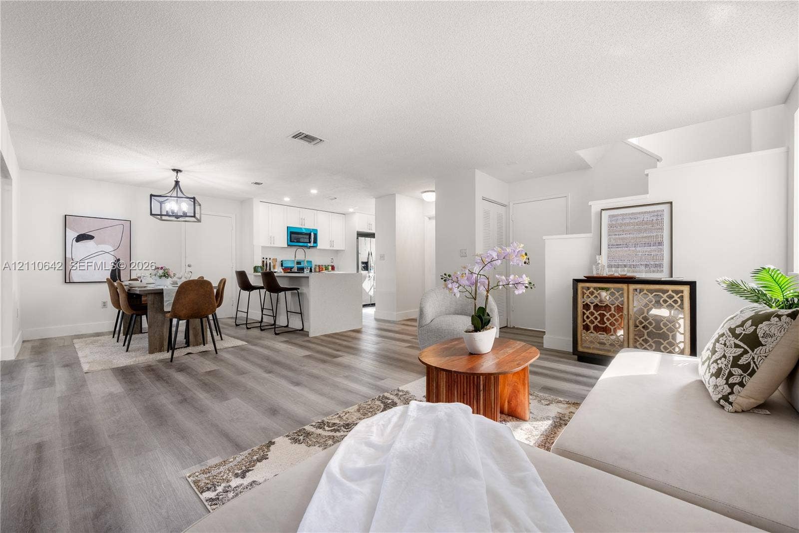 14732 SW 90th Terrace, Miami, FL 33196 Open-concept interior featuring wood-finish flooring, white cabinetry, a kitchen island with stone-surface countertop, and a contemporary geometric hanging light fixture