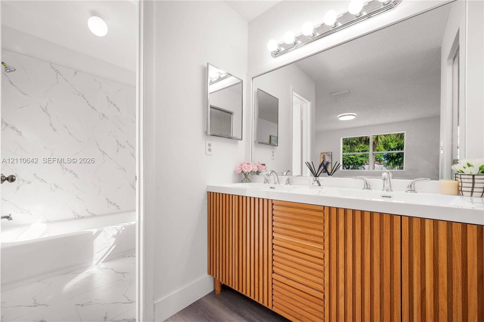 14732 SW 90th Terrace, Miami, FL 33196 Double vanity with slatted wood-finish cabinetry, integrated rectangular sinks, expansive wall-to-wall mirror, and floor-to-ceiling tilework featuring stone-patterned wall panels
