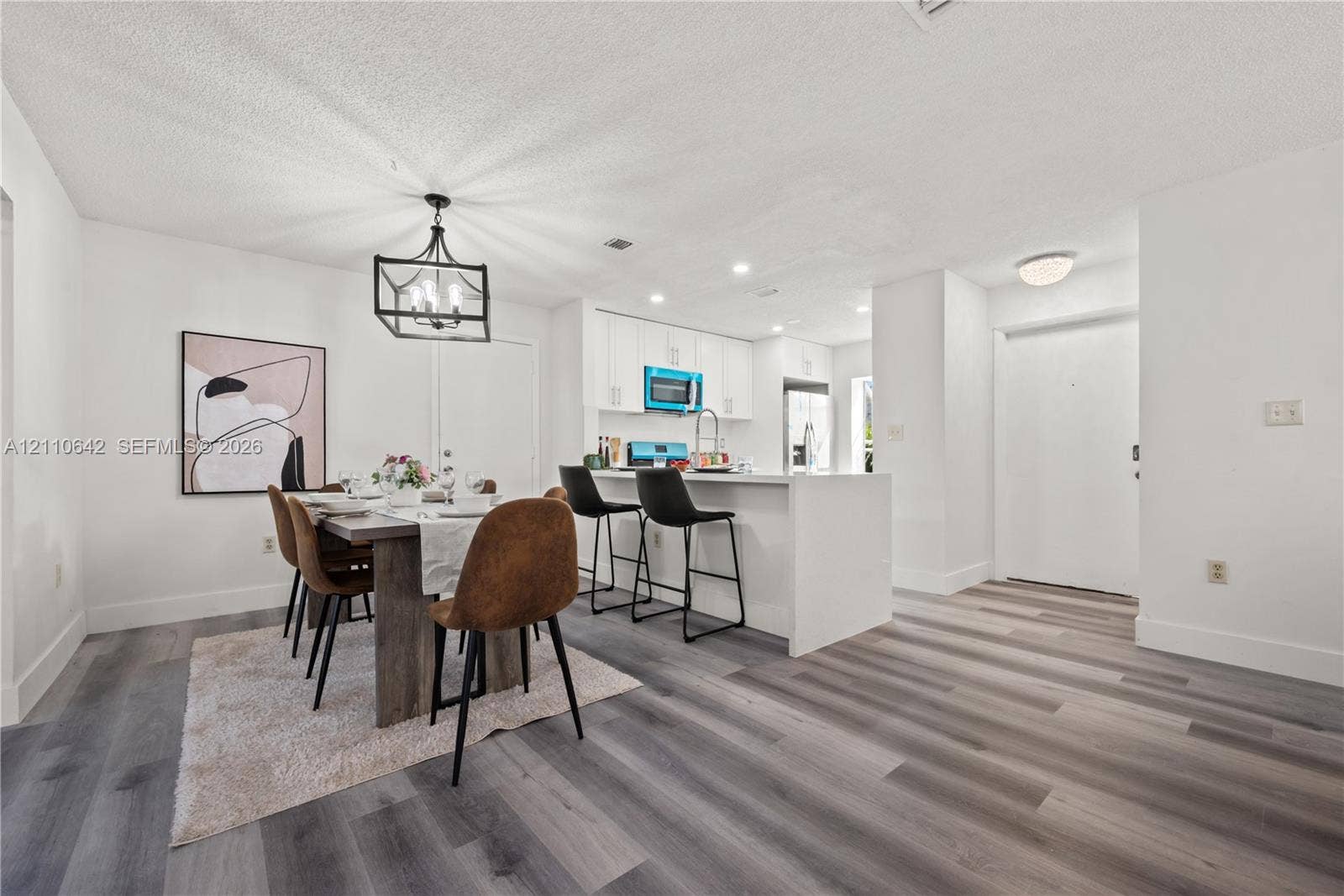 14732 SW 90th Terrace, Miami, FL 33196 Kitchen featuring white cabinetry, an island with stone-surface countertop, and wood-finish flooring throughout the space, accented by a geometric metal chandelier