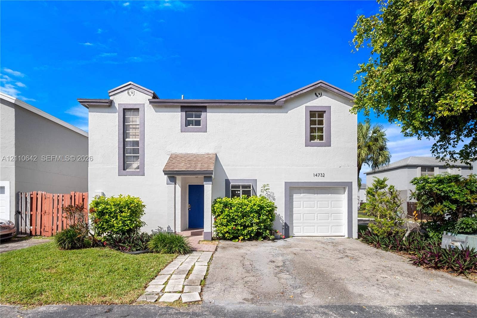 14732 SW 90th Terrace, Miami, FL 33196 Two-story stucco exterior featuring a built-in single-car garage, defined entryway with a gabled porch cover, stone-paver walkway, and mature landscaping