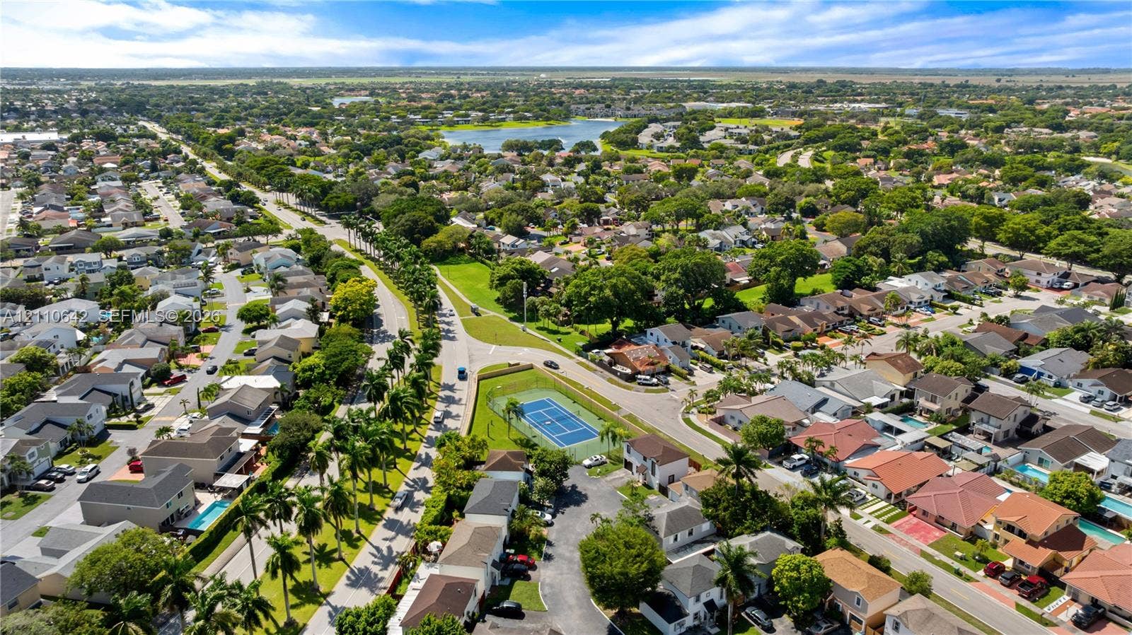 14732 SW 90th Terrace, Miami, FL 33196 Aerial perspective of a residential community featuring a fenced tennis court, mature landscaping, and proximity to a central lake