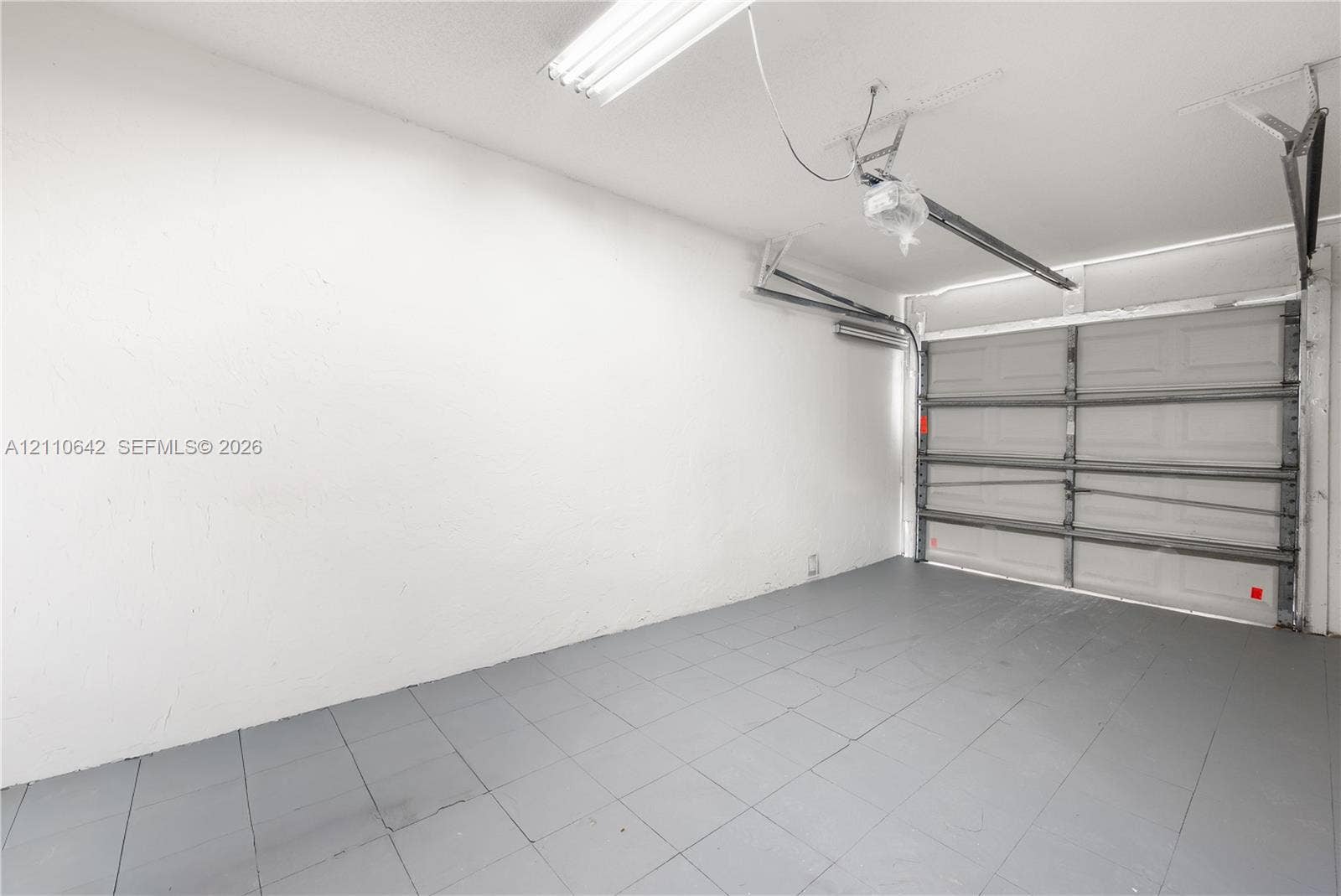 14732 SW 90th Terrace, Miami, FL 33196 Garage interior featuring a sectional overhead door, painted flooring, textured walls, and a ceiling-mounted lighting fixture