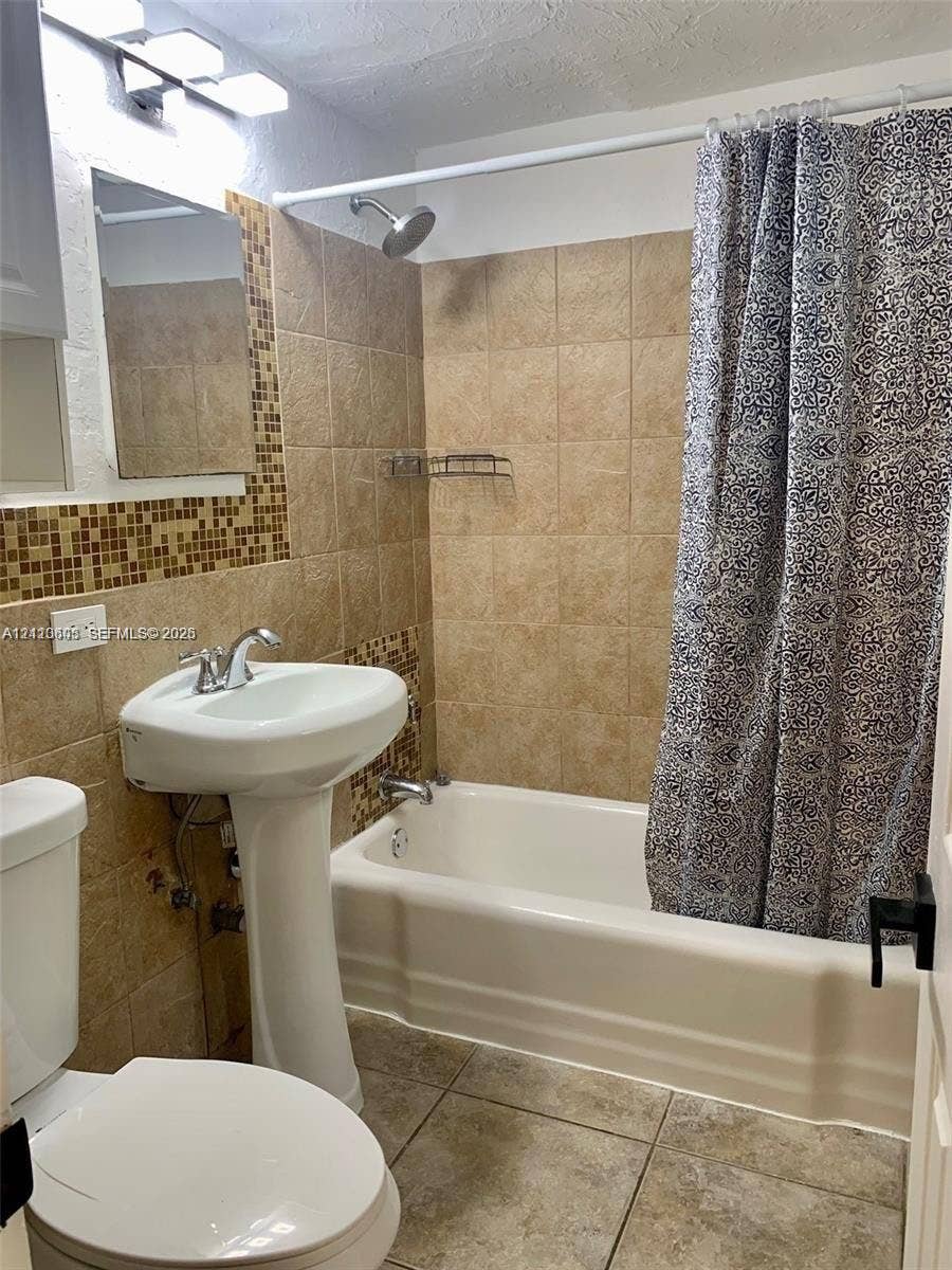 Pedestal sink with chrome faucet, shower-tub combination, ceramic wall tile surround with mosaic tile accents, and tiled flooring