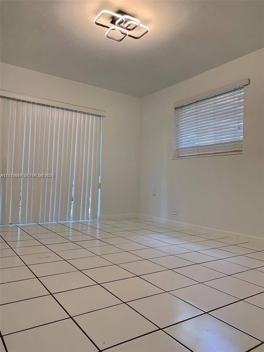 Neutral-toned room featuring large-format ceramic tile flooring, modern geometric LED flush-mount lighting, sliding glass patio doors, and horizontal window blinds