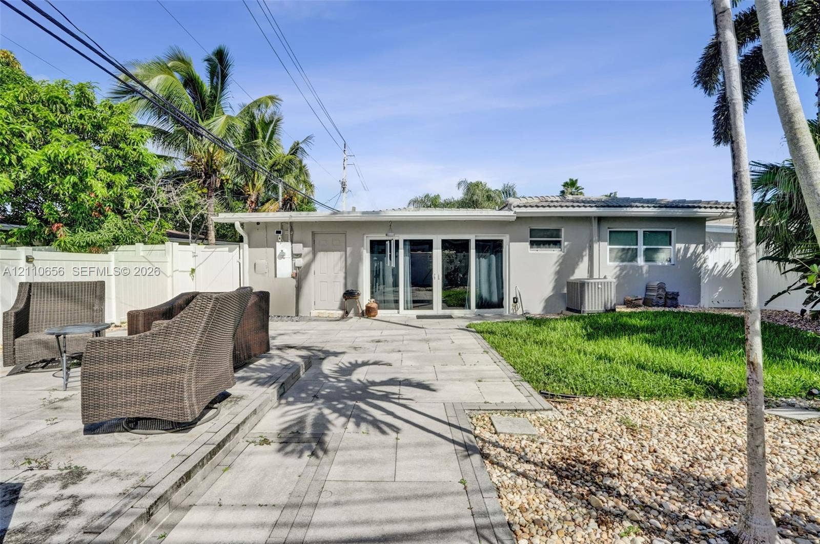 30 NE 48th Court, Oakland Park, FL 33334 Rear exterior featuring a concrete paver patio, sliding glass doors, a manicured lawn, and perimeter vinyl fencing