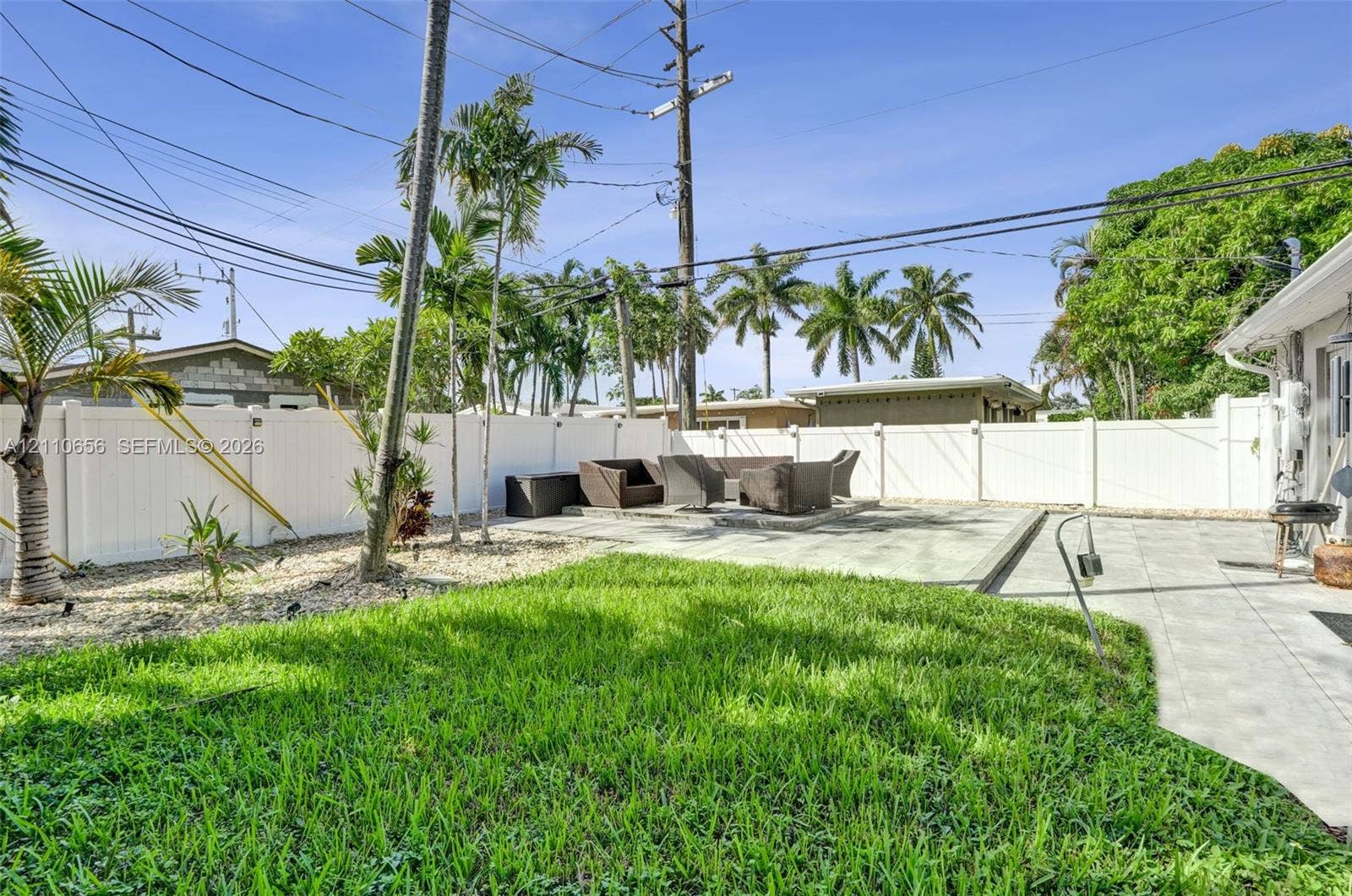 30 NE 48th Court, Oakland Park, FL 33334 Backyard featuring a paved patio, manicured lawn, white vinyl perimeter fencing, and mature palm trees