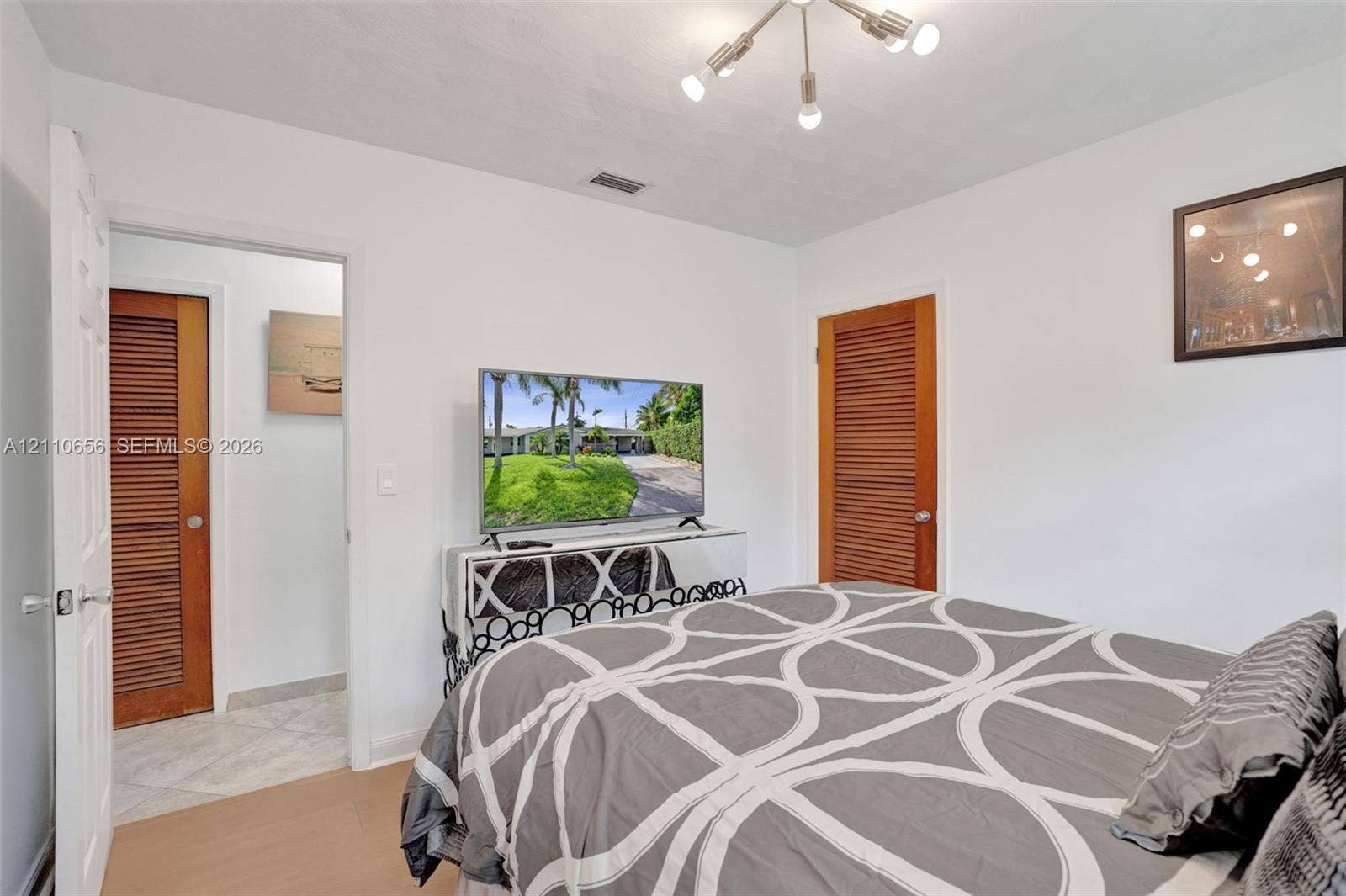 30 NE 48th Court, Oakland Park, FL 33334 Neutral interior featuring wood-finish flooring, a multi-arm modern light fixture, and dual wood-tone louvered doors