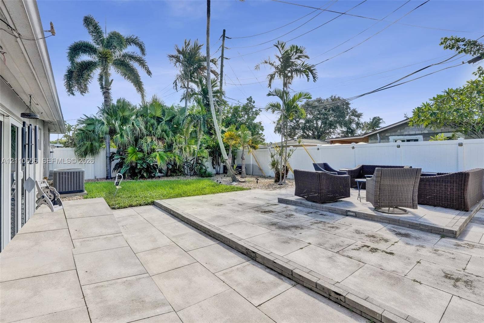 30 NE 48th Court, Oakland Park, FL 33334 Backyard featuring a split-level concrete paver patio, a grass lawn, mature palm trees, and perimeter vinyl fencing