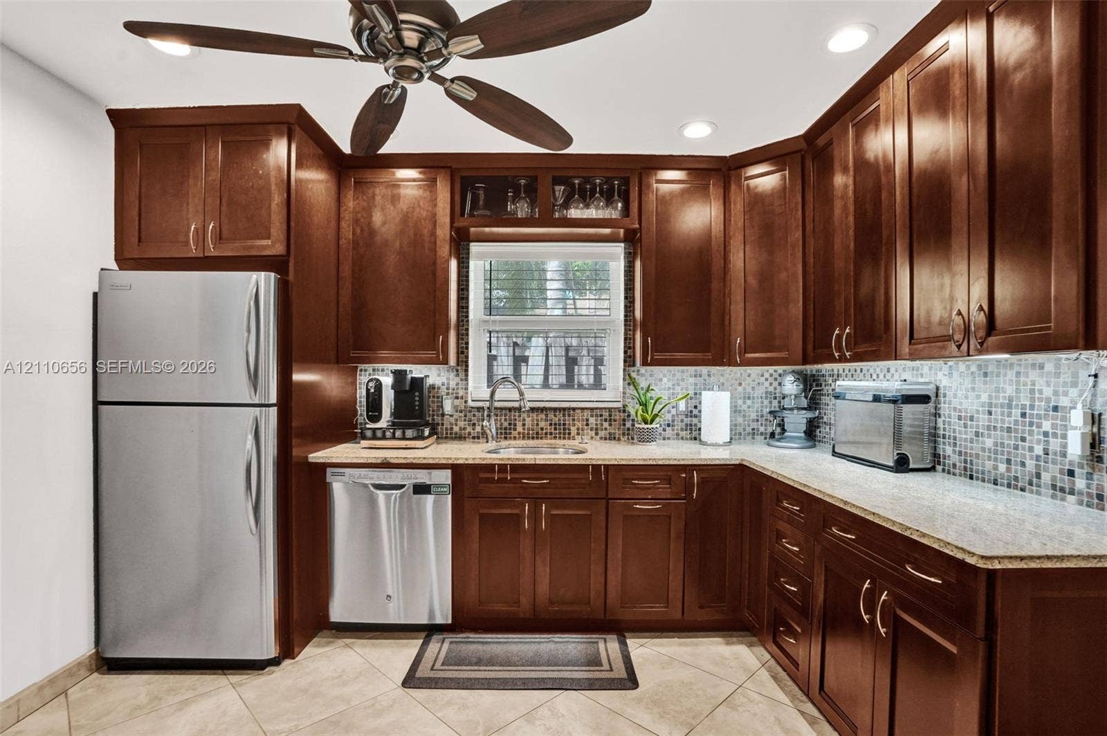 30 NE 48th Court, Oakland Park, FL 33334 Kitchen featuring stained-wood cabinetry, stone-finish countertops, mosaic tile backsplash, stainless steel appliances, and tile flooring