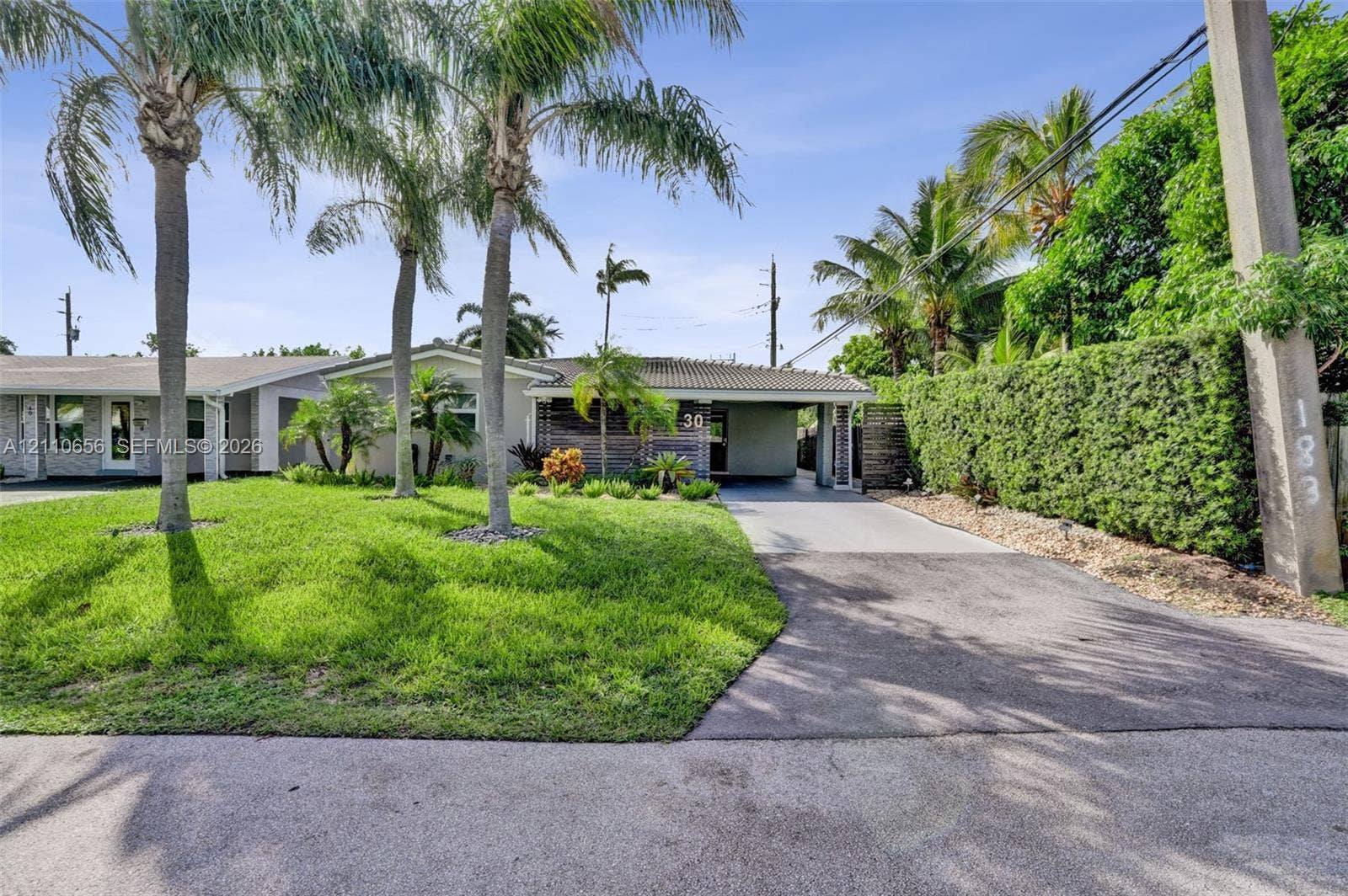 30 NE 48th Court, Oakland Park, FL 33334 Exterior featuring a concrete tile roof, paved driveway with an integrated carport, established palm trees, and manicured landscaping