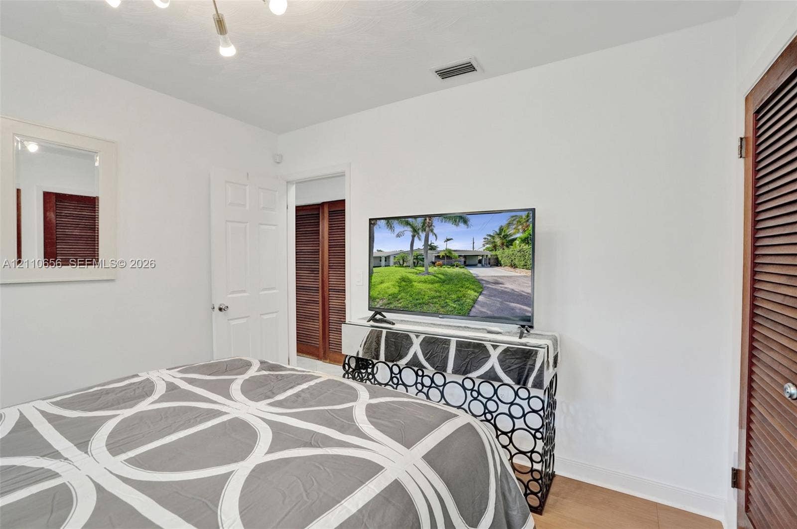 30 NE 48th Court, Oakland Park, FL 33334 Neutral-toned room featuring a multi-light fixture, crisp white walls, and wood-finish doors with louvered detailing