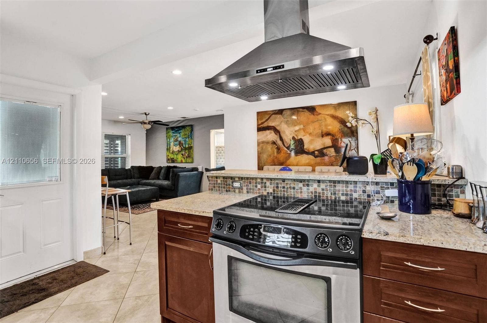 30 NE 48th Court, Oakland Park, FL 33334 Kitchen featuring dark-finish cabinetry, stone-style countertops, mosaic tile backsplash, and a stainless steel range hood