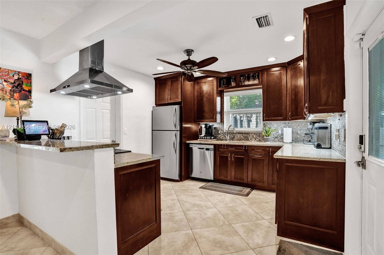 30 NE 48th Court, Oakland Park, FL 33334 Kitchen featuring dark wood cabinetry, stone countertops, a mosaic tile backsplash, stainless steel appliances, and a ceiling-mounted stainless steel vent hood