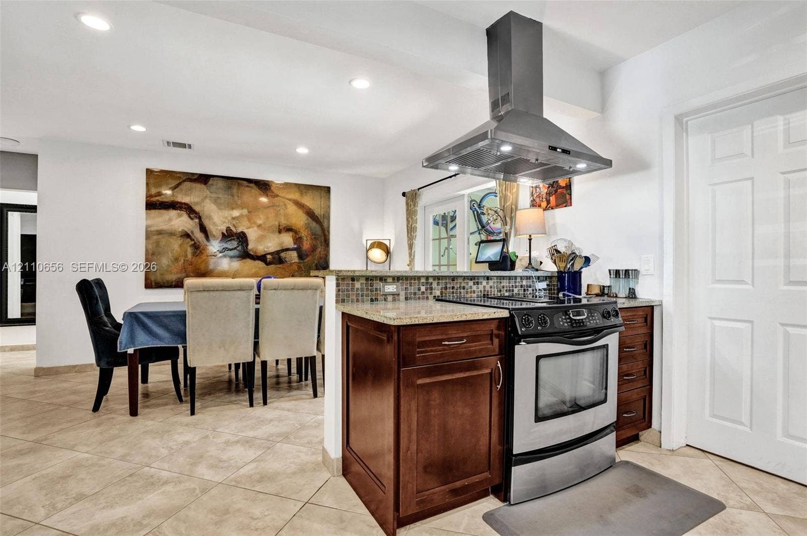 30 NE 48th Court, Oakland Park, FL 33334 Kitchen featuring dark wood cabinetry, stone-finish countertops, mosaic tile backsplash, stainless steel range, and stainless steel chimney-style range hood