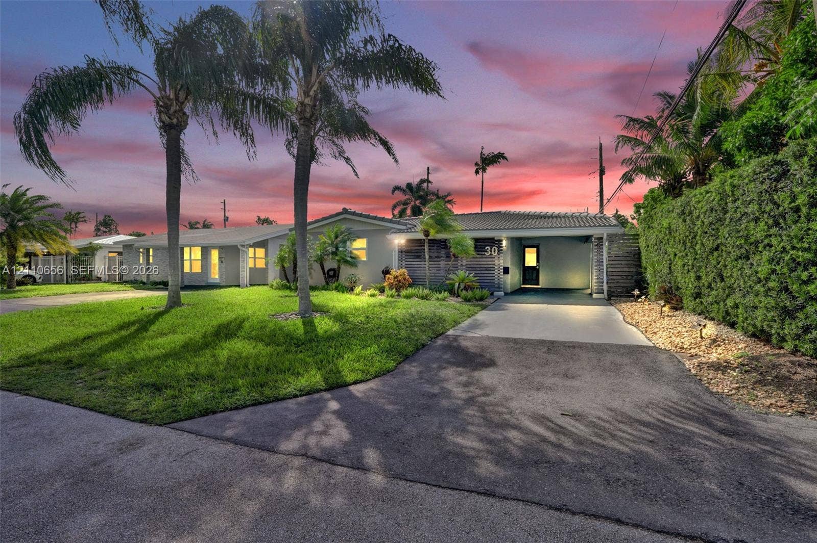 30 NE 48th Court, Oakland Park, FL 33334 Single-story exterior featuring a concrete tile roof, integrated carport, manicured lawn, and established palm trees