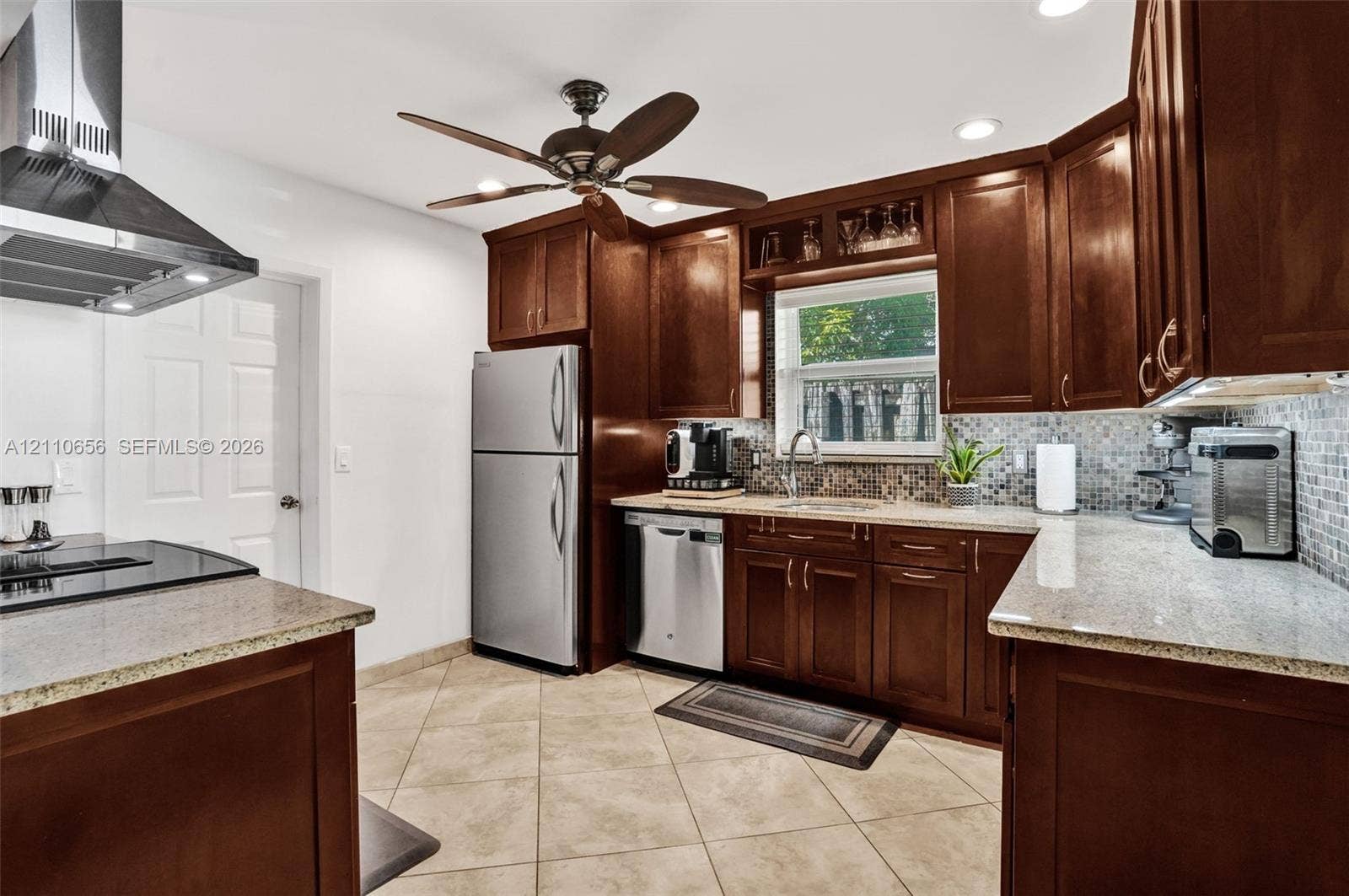 30 NE 48th Court, Oakland Park, FL 33334 Kitchen featuring dark wood cabinetry, stone countertops, stainless steel appliances, a mosaic tile backsplash, and ceramic tile flooring