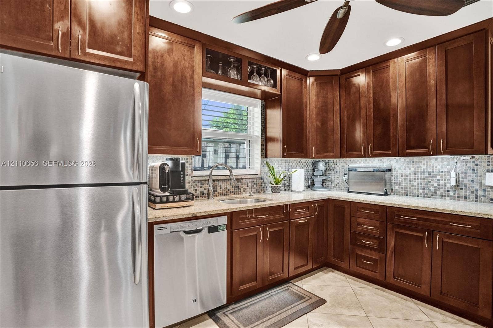 30 NE 48th Court, Oakland Park, FL 33334 Kitchen featuring raised-panel wood cabinetry, glass-front upper cabinet detailing, stainless steel appliances, stone-look countertops, and a multi-tonal mosaic tile backsplash