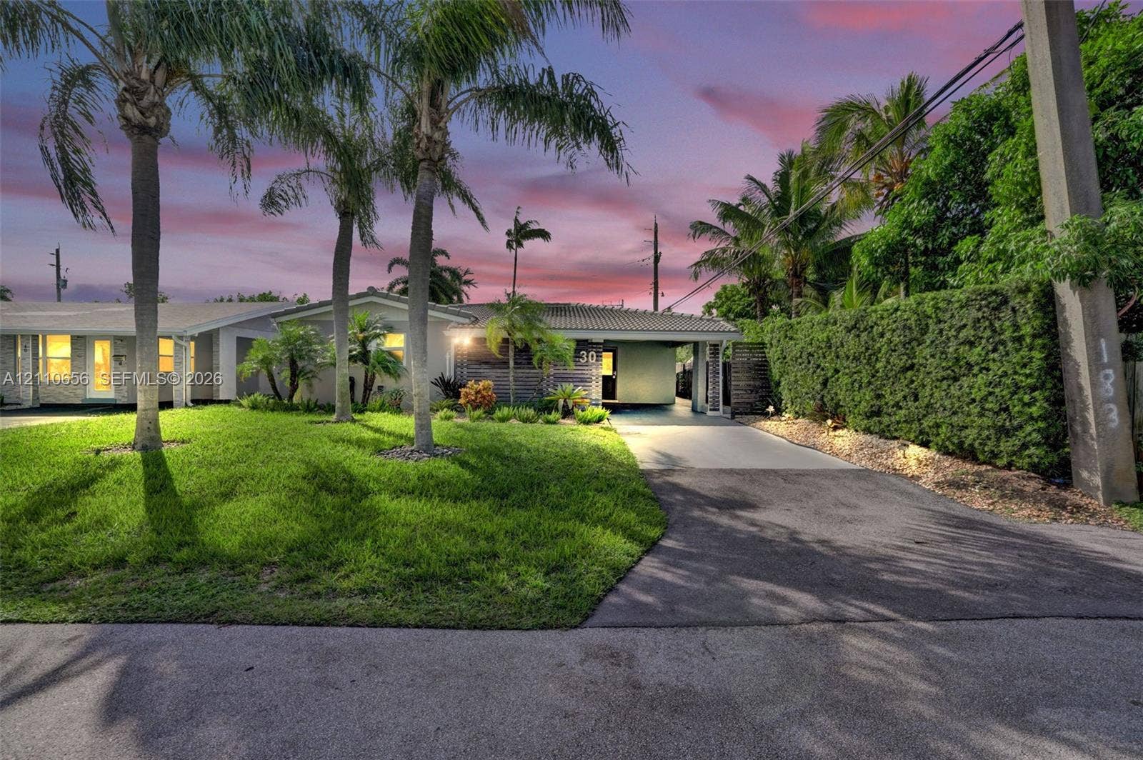 30 NE 48th Court, Oakland Park, FL 33334 Single-story exterior featuring a concrete tile roof, attached covered carport, paved driveway, and mature landscaping