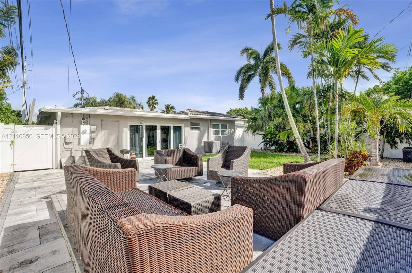 30 NE 48th Court, Oakland Park, FL 33334 Expansive outdoor living area featuring paved patio flooring, a white privacy fence, and mature palm trees