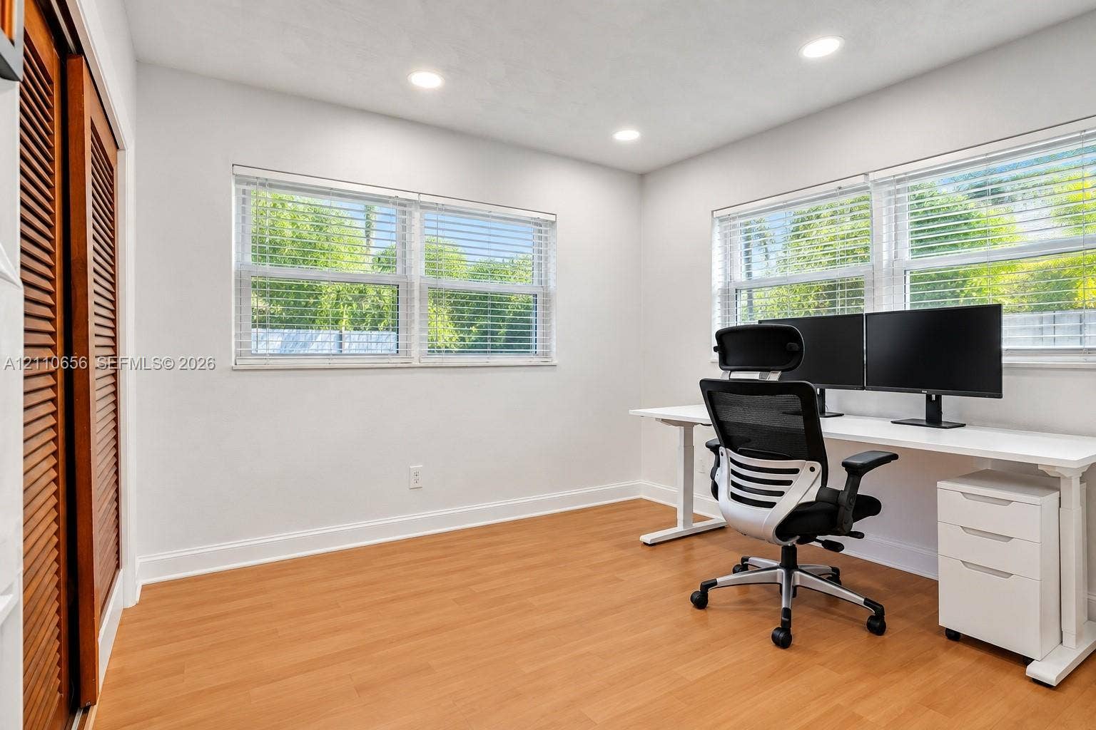 30 NE 48th Court, Oakland Park, FL 33334 Room featuring wood-finish flooring, recessed lighting, dual windows with horizontal blinds, and a closet with louvered doors
