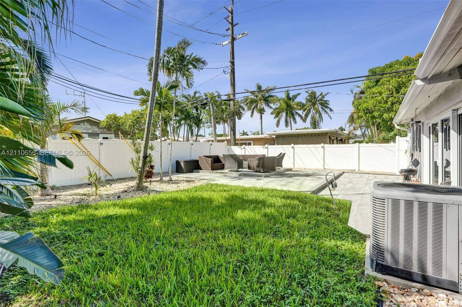 30 NE 48th Court, Oakland Park, FL 33334 Backyard featuring a paved patio area, manicured lawn, stone landscape accents, and a perimeter vinyl privacy fence