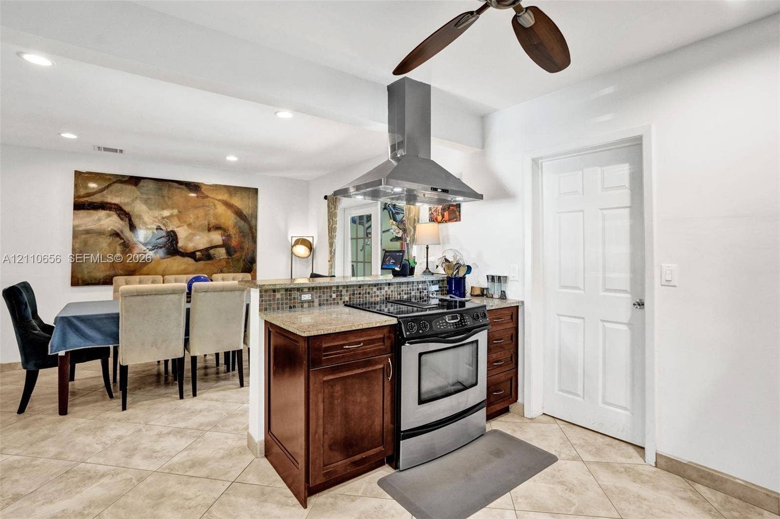 30 NE 48th Court, Oakland Park, FL 33334 Kitchen featuring dark wood cabinetry, stone countertops, mosaic tile backsplash, stainless steel range with overhead vent hood, and tile flooring