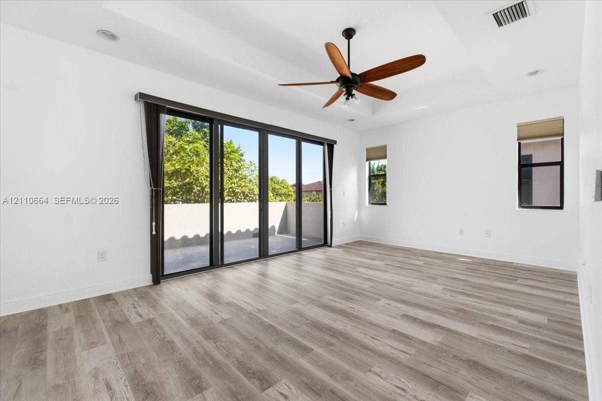 An elegant tray ceiling adds architectural distinction, while expansive multi-panel glass doors fill the space with natural light, providing access to a private balcony