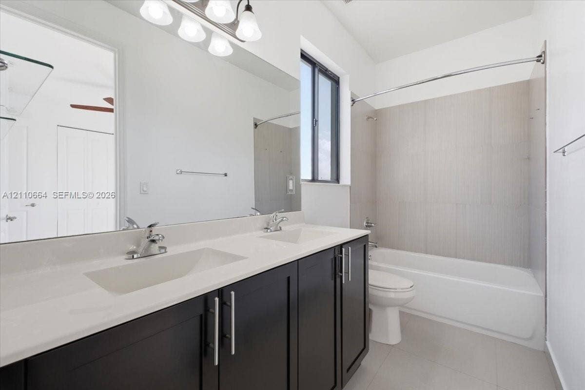Jack-and-Jill bathroom featuring a dual-sink vanity, dark cabinetry, full-width mirror and tiled bathtub.