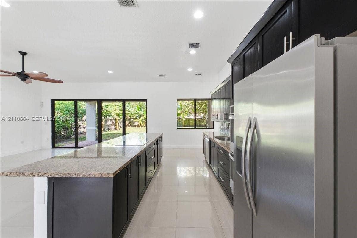 Spacious kitchen with a generous center island housing a new induction cooktop, granite countertops, rich dark cabinetry, double wall ovens, stainless steel refrigerator and dishwasher, recessed lighting, and tile flooring