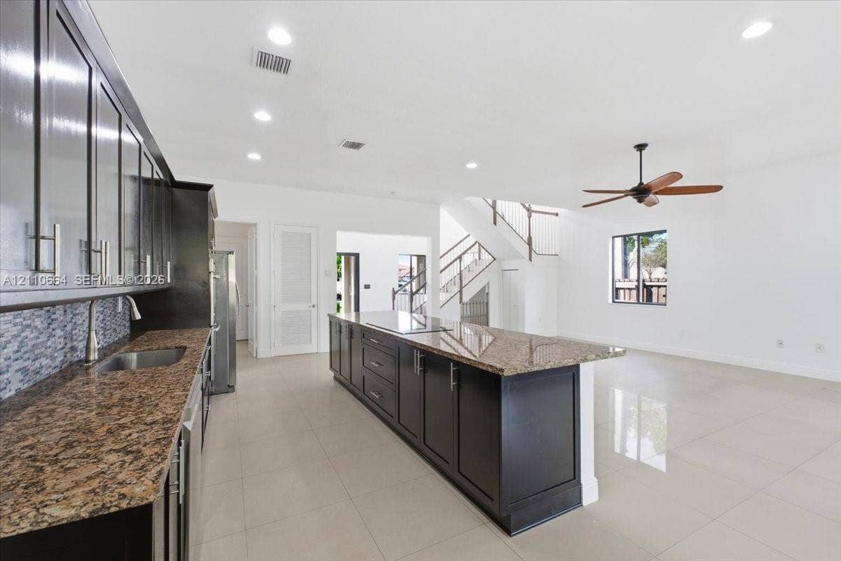 Spacious kitchen with a generous center island housing a new induction cooktop, granite countertops, rich dark cabinetry, double wall ovens, stainless steel refrigerator and dishwasher, recessed lighting, and tile flooring