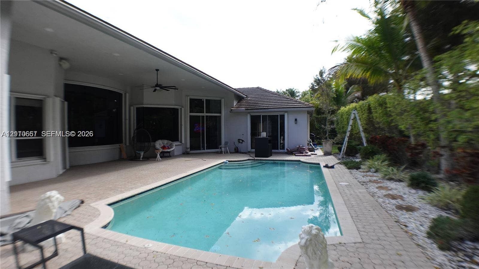 Rear exterior featuring an in-ground swimming pool, concrete paver patio, covered porch with a ceiling fan, and stucco siding