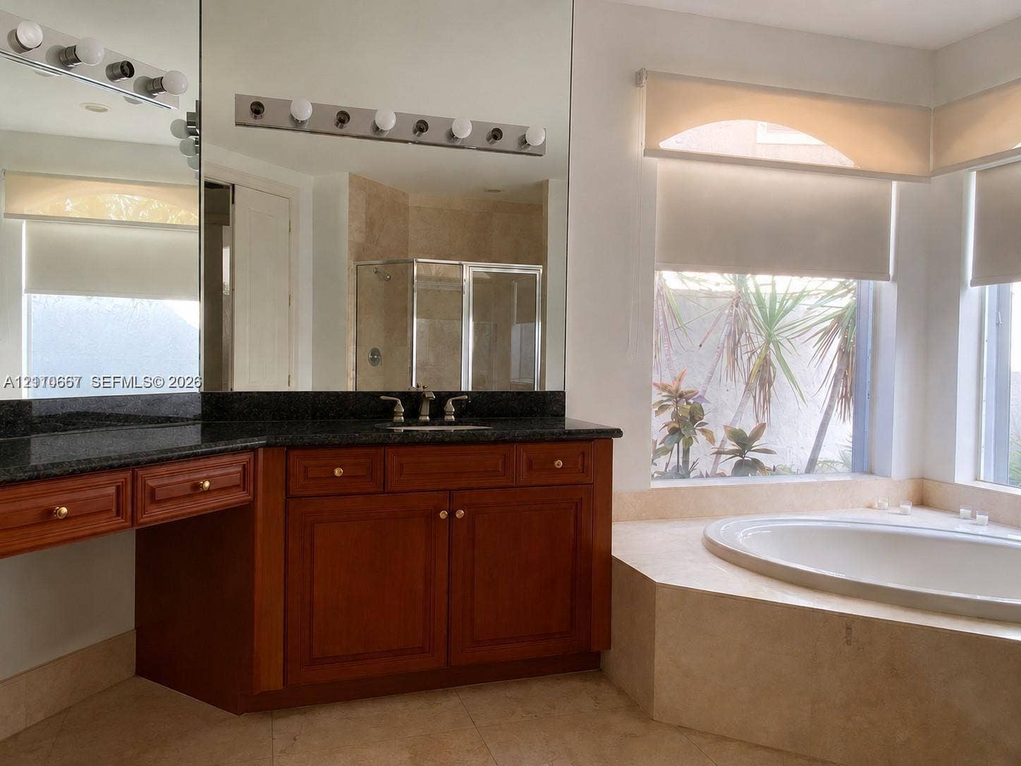 Double vanity featuring integrated sinks, stone-surface countertop, white cabinetry, large wall-mounted mirror, and tile flooring laid on a diagonal