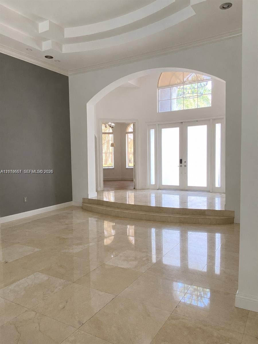 Interior space featuring multi-tiered tray ceiling, large-format polished stone flooring, expansive floor-to-ceiling windows, recessed lighting, and arched architectural detailing