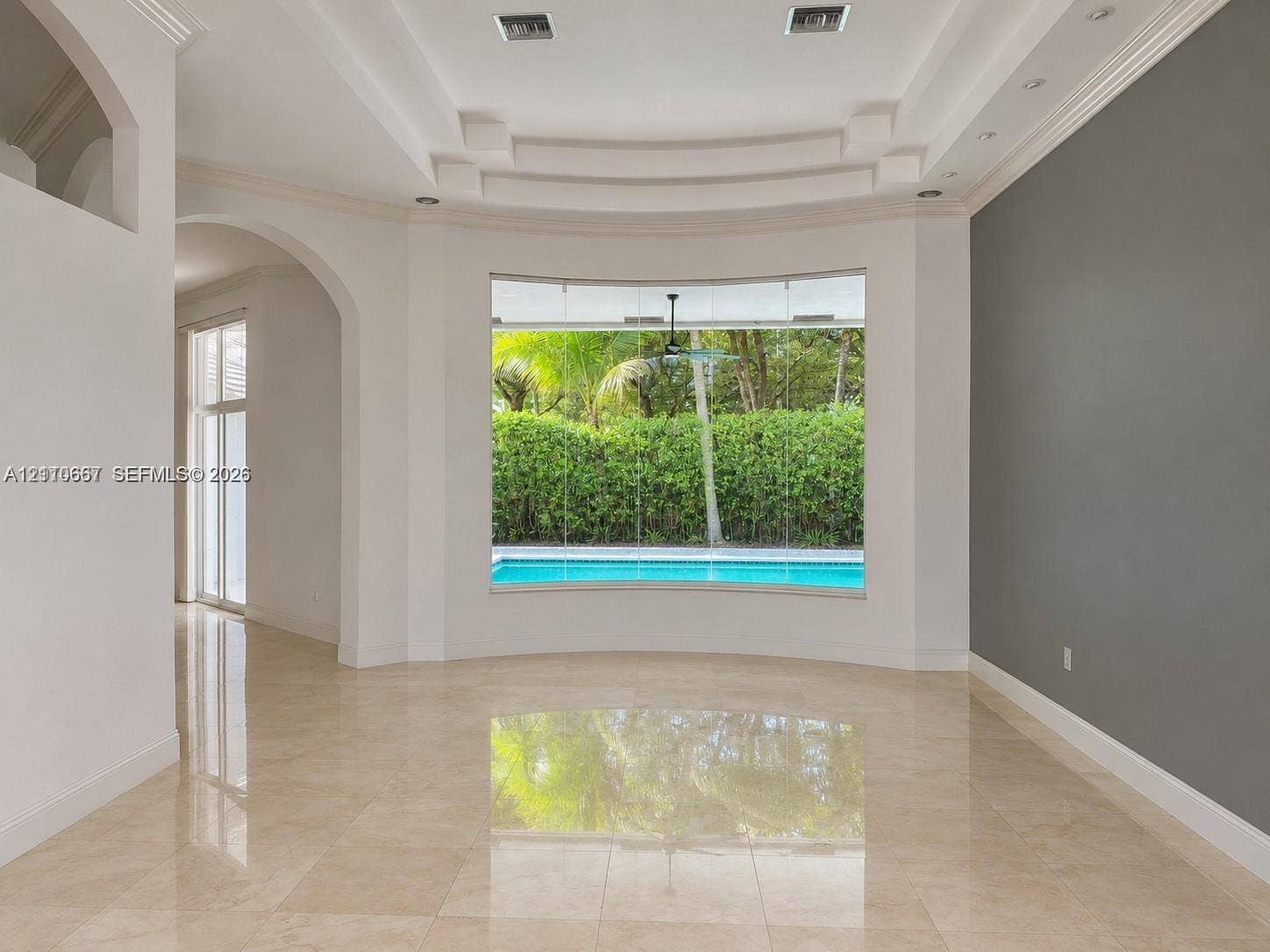 Interior space featuring polished stone flooring, recessed tray ceiling with architectural molding, and an arched entry