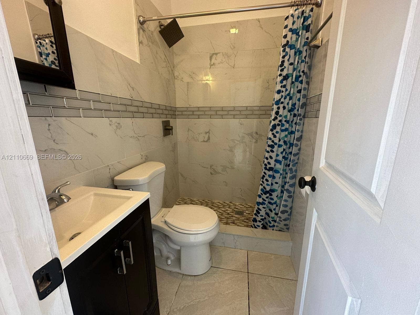 1635 Hollywood Boulevard, #B, Hollywood, Hollywood, FL 33020 Bathroom featuring a dark-finish vanity with a chrome faucet, large-format wall tile with decorative glass mosaic inlay, a walk-in shower with stone-style flooring, and a fixed rain-style showerhead