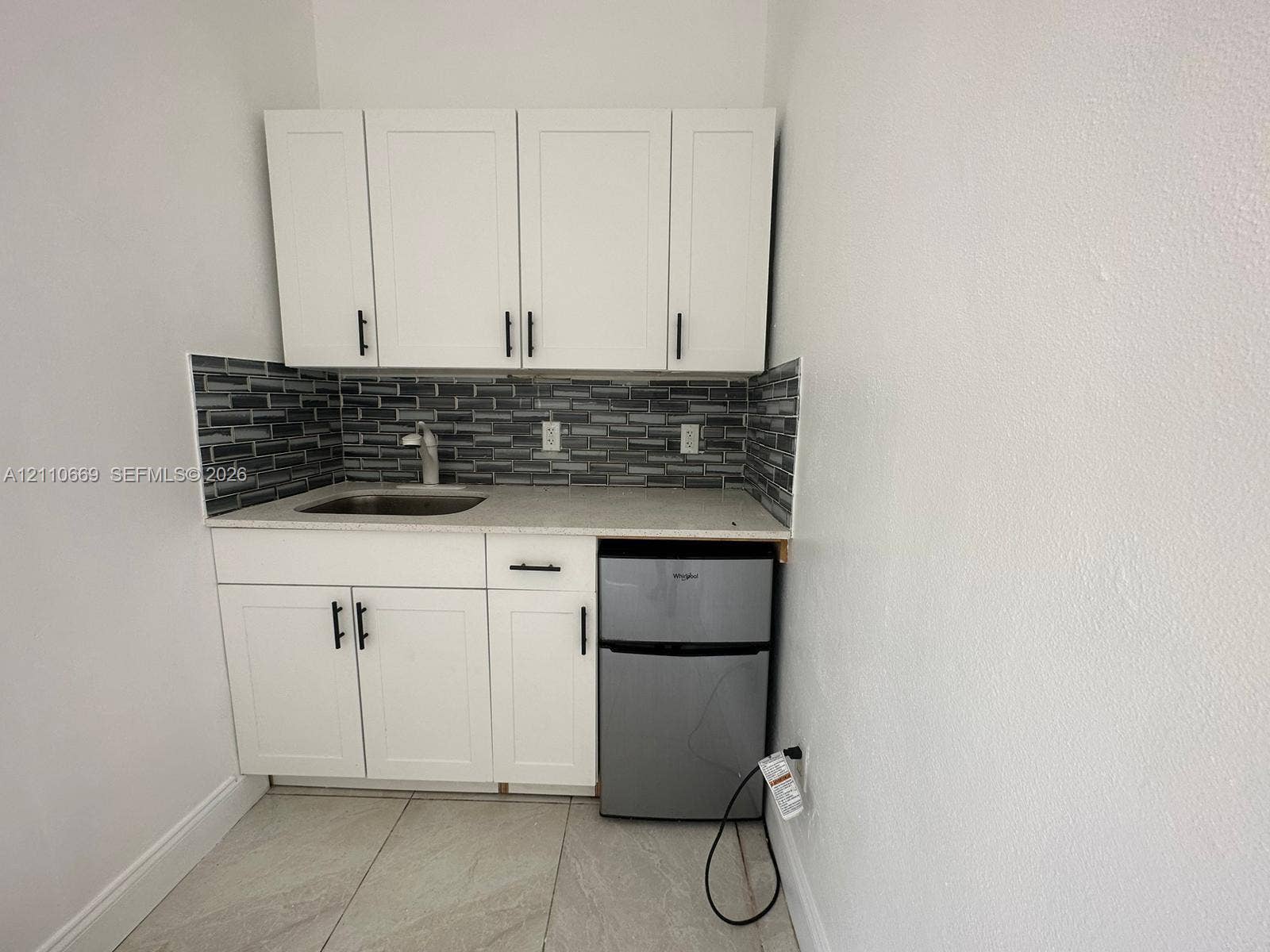 1635 Hollywood Boulevard, #B, Hollywood, Hollywood, FL 33020 Kitchenette featuring white cabinetry with matte black hardware, stone-finish countertop, stainless steel sink with high-arc faucet, linear mosaic tile backsplash, and built-in under-counter refrigerator