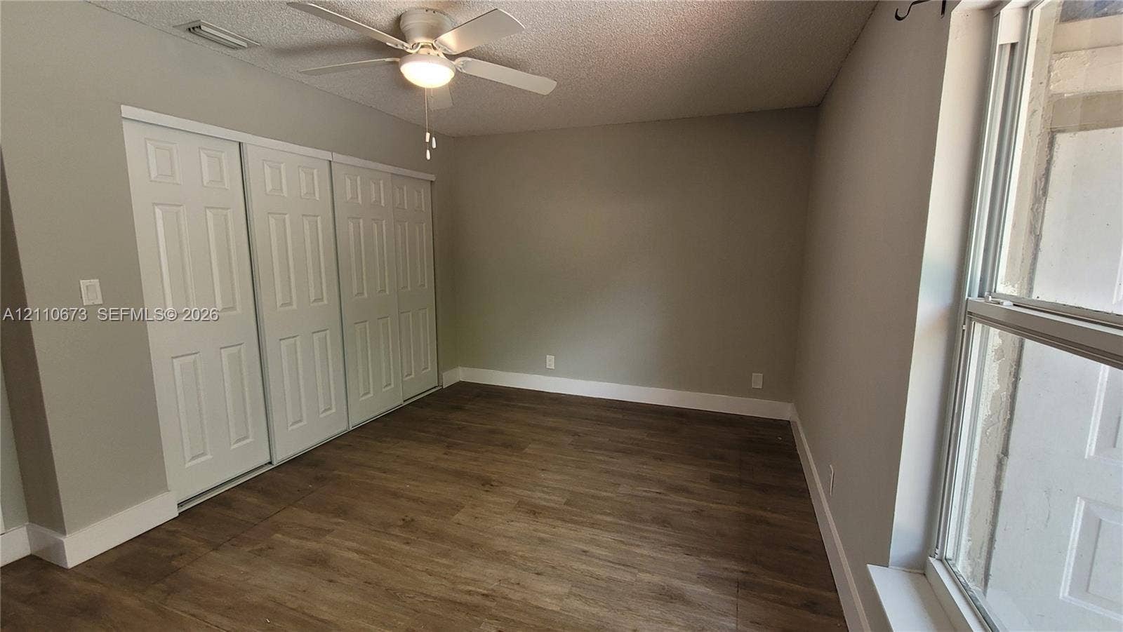 Wood-finish flooring, multi-panel sliding closet doors, ceiling fan with integrated light fixture, and large window with natural lighting