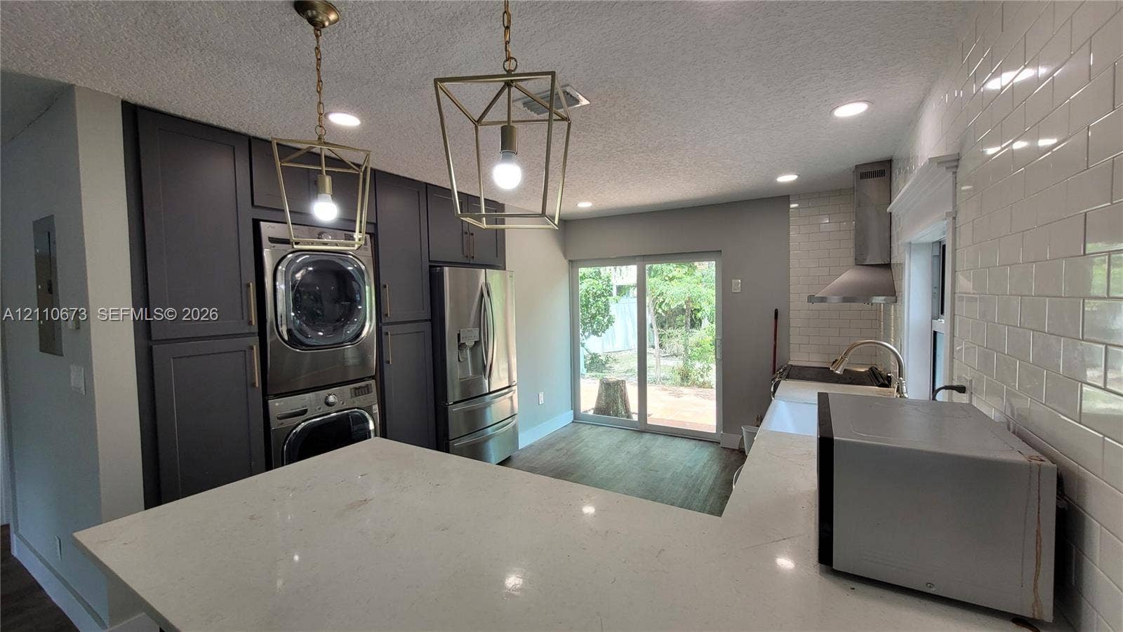 Kitchen featuring quartz countertops, white subway tile backsplash, dark-toned cabinetry, stainless steel appliances, and geometric pendant lighting
