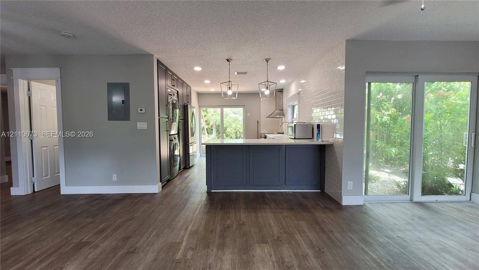 Kitchen featuring a central island with cabinetry, subway tile backsplash, stainless steel range hood, and wood-finish flooring