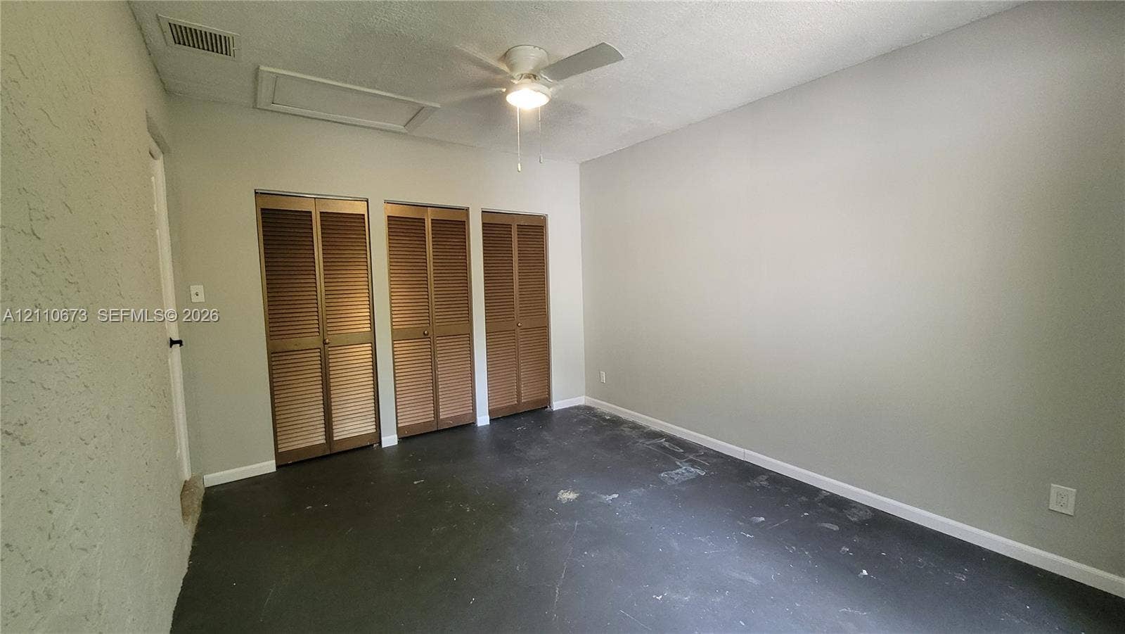 Interior space featuring three bi-fold louvered closet doors, a white ceiling fan with integrated lighting, and textured wall finish