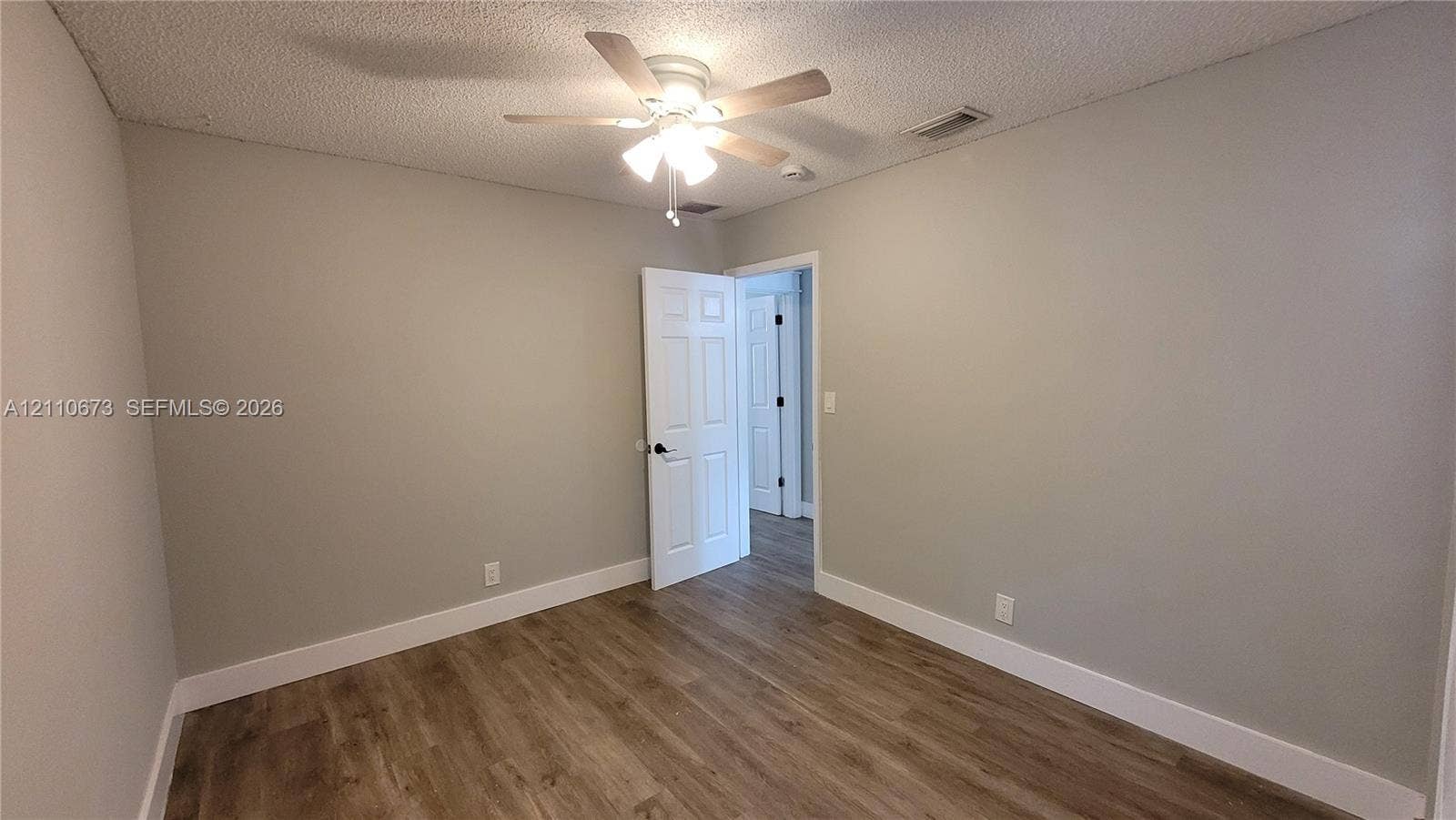 Room interior featuring wood-finish flooring, neutral wall paint, and a ceiling-mounted light fixture with a fan