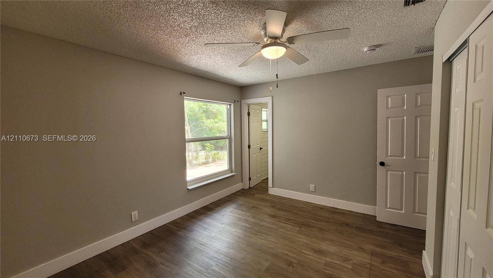 Room featuring wood-finish flooring, a ceiling fan with integrated lighting, a single-pane window, and white paneled doors