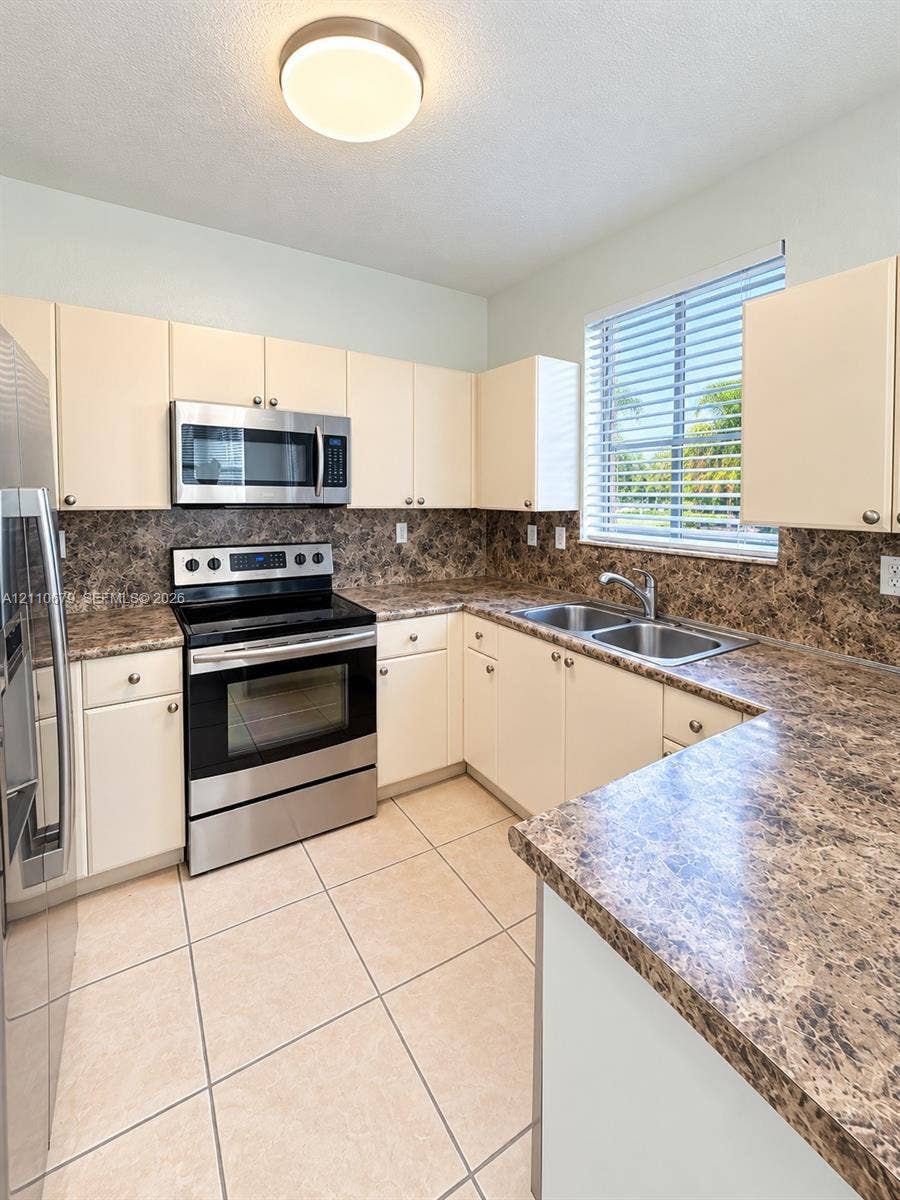 Kitchen featuring flat-panel cabinetry, stone-patterned laminate countertops, stainless steel appliances, a double-basin stainless steel sink, and ceramic tile flooring