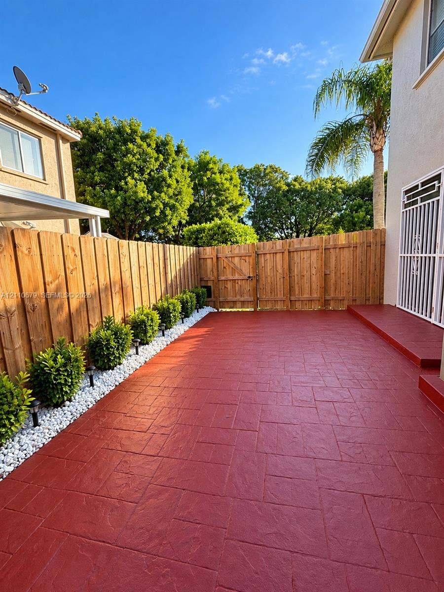 Stamped concrete patio featuring a perimeter of white decorative stones, integrated shrubbery, a wood privacy fence, and a metal security door