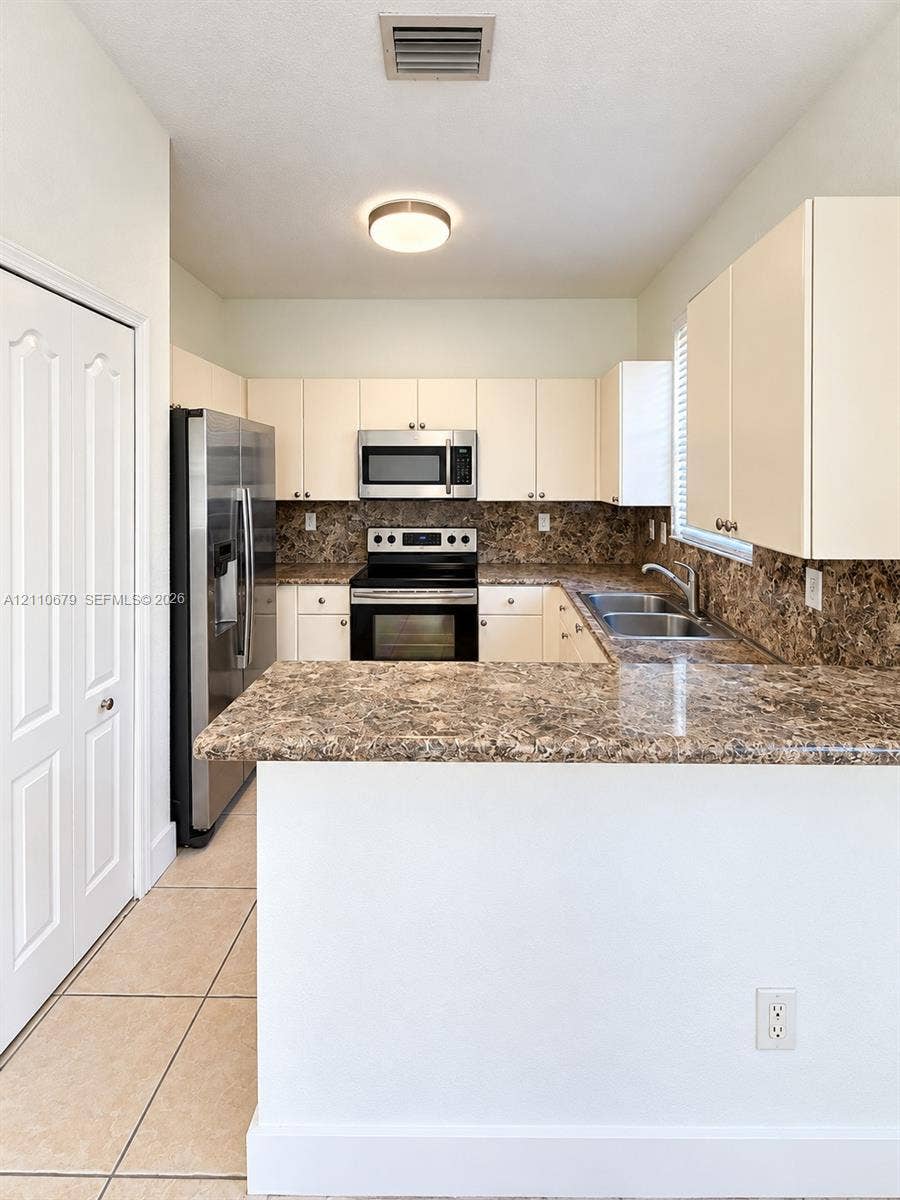 Kitchen featuring solid-surface countertops, stainless steel appliances, flat-panel cabinetry, and tile flooring