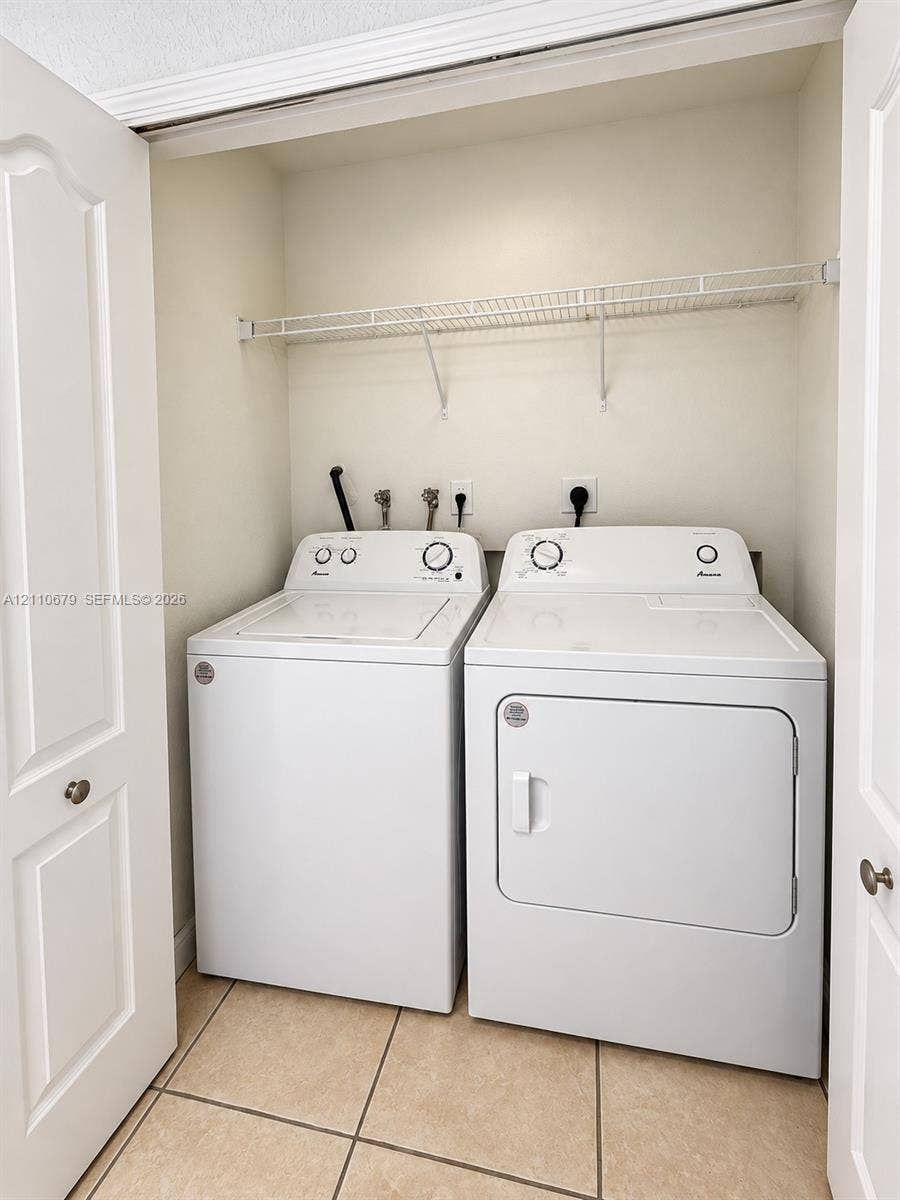 Laundry closet featuring tile flooring, white bi-fold doors, and a wall-mounted wire storage shelf