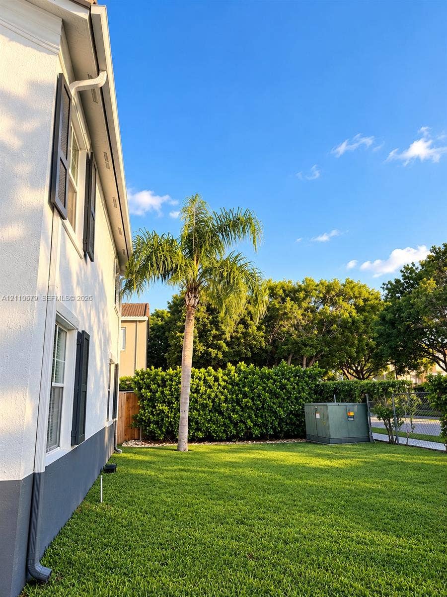 Exterior side yard featuring stucco siding, two-tone paint, dark shutters, manicured lawn, and mature landscaping