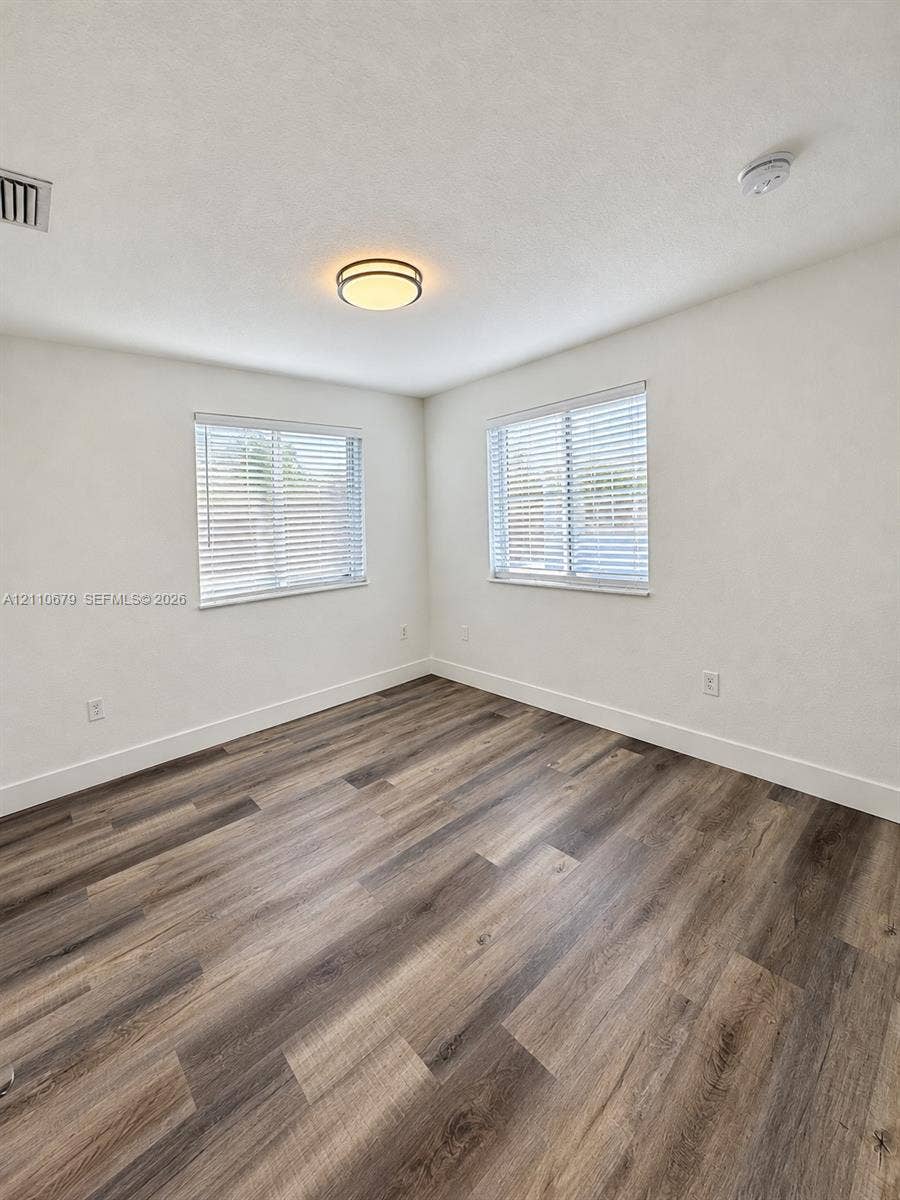Room featuring wood-finish flooring, dual windows with blinds, and a central flush-mount light fixture