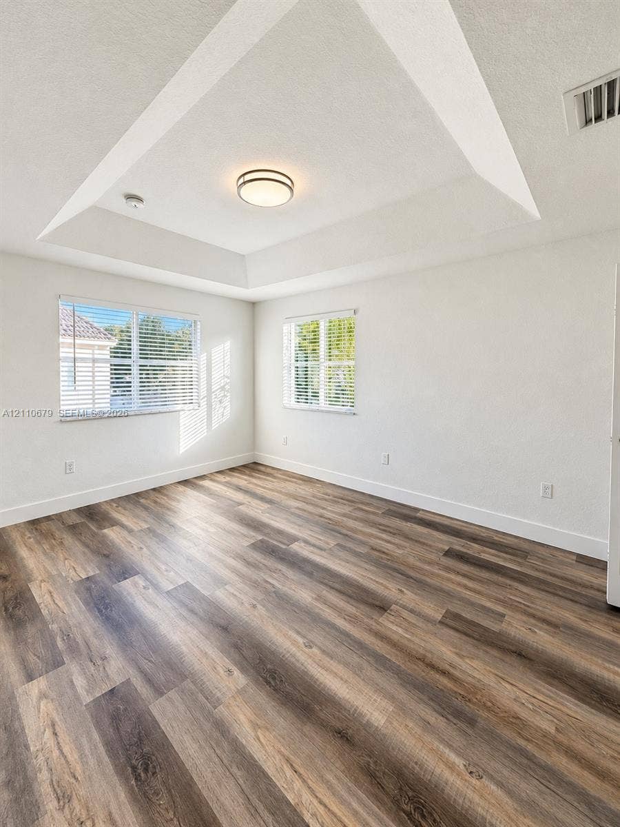 Tray ceiling, wood-finish flooring, and dual windows with fitted blinds