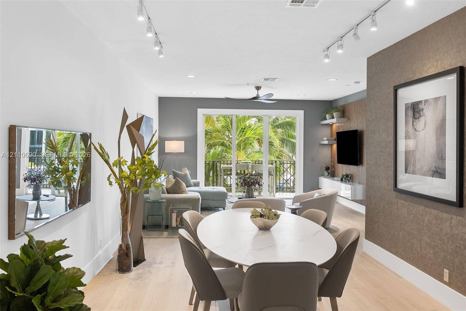Living area featuring light-toned wood-finish flooring, adjustable track lighting, a textured accent wall, integrated floating shelving, and a glass-paneled sliding door